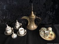 Overall lot showing brass dallah, three metal-ceramic cup sets, and porcelain pieces on tray