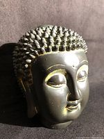 Front three-quarter view of bronze Buddha head showing facial detail and patina