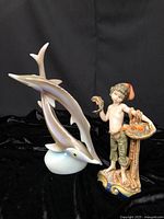 Double sturgeon porcelain figurine and boy with fish basket figurine side by side