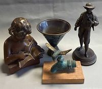 Group shot of four vintage metal items: standing boy figure, reading girl bust, bird faucet, green bowl