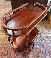 Oblique view showing top spindle-railed tray, lower shelf, large wheel, handle