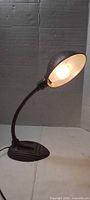 Front view of the lamp illuminated showing shade, gooseneck and base