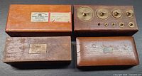 Top view of four wooden scientific boxes including hydrometer cases, weight holder with brass weights visible, and small instrument box