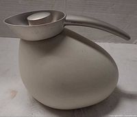 Side profile of Georg Jensen Quack jug showing asymmetrical beige body and stainless steel handle-spout