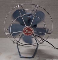 Front view of Torcan blue metal desk fan showing chrome guard and logo