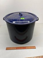 Front view of dark blue speckled enamelware pot with lid and ruler for scale