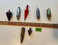 Seven plumb bobs laid out with ruler for scale