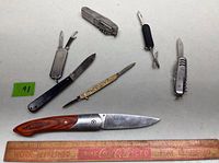 All seven pocket knives and multi-tools laid out on table with blades/tools open for visibility