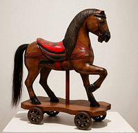 Full view of carved wooden horse on wheeled base, gallery setting