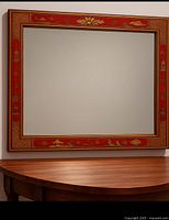 Front view of rectangular red lacquer Chinoiserie mirror above wooden surface