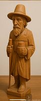 Front view of carved wooden traveler holding staff and jug