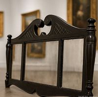 Front view of triple-panel mirror propped on floor showing carved crest, columns, beveled glass