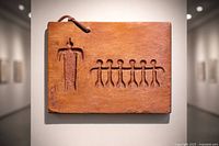 Front view of plaque showing carved figures and leather strap