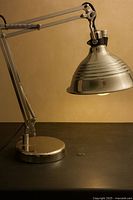 Full view of chrome task lamp on surface showing articulated arm, ribbed shade, weighted base