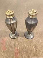 Two silver-plated shakers standing upright showing tarnish and wear
