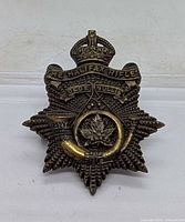 Front view of brass Halifax Rifles cap badge showing crown, motto and bugle horn
