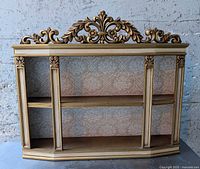 Front view of Syroco gold gilt curio shelf showing ornate crest, columns, shelves and damask back