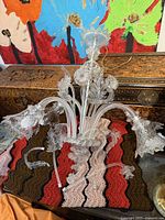 Partially assembled clear glass chandelier showing arms and floral shades on crocheted mat