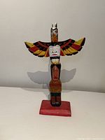 Front view of carved wood Indigenous totem pole on red base