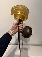Hand holding bronze-tone wall sconce with amber spiral glass shade
