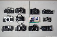 Top-down view of all ten cameras and flash laid out on table