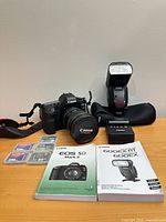 Overall shot of camera with lens, flash, charger, memory cards, manuals