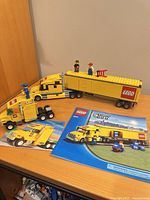 Both assembled yellow LEGO semi-trucks, trailers, minifigures and manuals displayed on tabletop