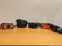 Four compact digital cameras with accessories aligned on surface