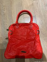 Front view of red Steve Madden tote showing overall design, handles, brand plaque, side zippers
