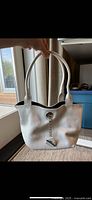 Front view of white leather bucket purse with handles and charm
