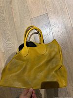 Front view of mustard yellow leather purse showing pebbled texture and handles