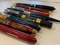 Side view of eleven pens laid in a row showing colors and finishes