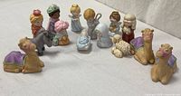 Group shot of all fourteen porcelain nativity pieces arranged in circle on white surface