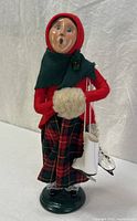 Front view of Byers’ Choice winter girl figurine showing snowball, skates, plaid skirt and green base