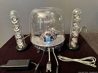Front view of full Harman Kardon SoundSticks system showing subwoofer, two satellites, power adapter and cables