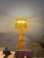 Full view of illuminated amber acrylic table lamp on glass surface