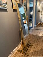 Side view of freestanding brass cheval mirror showing frame, base and finials