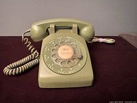 Front view of olive green rotary telephone showing dial and handset
