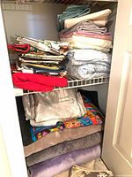 Closet shelf with stacks of sheets, blankets and tea towels