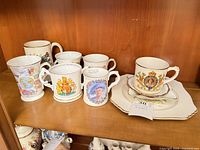 Seven mugs, teacup on saucer and square plate displayed on shelf