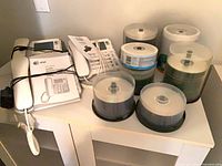 Two AT&T large button phones, manual, power adapter, and six disc spindles on shelf