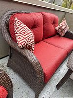Brown wicker loveseat with red cushions and accent pillow