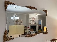 Full view of rectangular mirror on wall showing gold appliqués and living room reflection