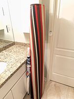 Rolled striped outdoor rug standing upright beside umbrella