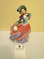 Front view of Royal Doulton "Autumn Breezes" figurine with auction card showing height