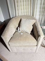 Front view of beige upholstered swivel arm chair with cushion and pillow