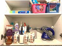 Cabinet shelf with steam cleaner, lint rollers, spray cleaners, dish soap, microfiber cloths
