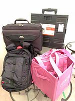 Group shot of backpack, briefcase, rolling crate and pink collapsible tote with shopping bags
