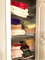 Three closet shelves filled with folded towels in various colors
