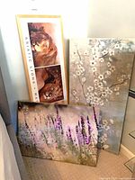 Three wall art pieces leaning against wall: Asiatic Lions framed print, wildflower canvas, blossom canvas